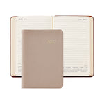 A 2027 daily planner shown open in the background with lined pages, with a closed textured leather cover in front. The cover is a warm taupe-beige color with '2027' embossed in gold.