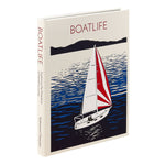 A hardcover book titled "BOATLIFE" standing upright at a slight angle. The cover features a stylized illustration of a sailboat on blue water with dark land silhouettes, and the spine repeats the title and author text.