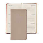 A 2027 daily planner shown closed in front of an open version of the same planner. The closed planner has a textured light beige cover with gold foil '2026' lettering.