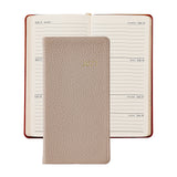 A 2027 daily planner shown closed in front of an open version of the same planner. The closed planner has a textured light beige cover with gold foil '2026' lettering.